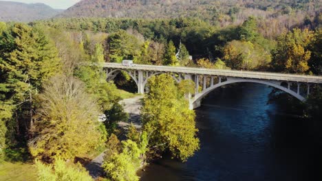 Aerial-frowarding-shot-of-a-bridge-over-Housatonic-river-passing-with-the-view-of-a-white-van-passing-by-on-a-hilly-terrain-in-Litchfield-County,-Connecticut,United-States