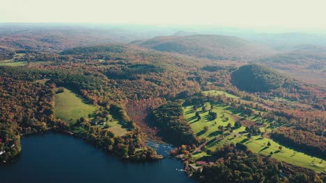 Beautiful-drone-shot-over-the-countryside-landscape-with-the-blue-lake-surrounded-by-hilly-terrain-covered-by-dense-green-vegetation-in-Litchfield-county,-Connecticut,United-States