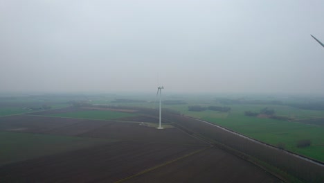 Drohne,-Die-In-Der-Nebligen-Holländischen-Landschaft-Auf-Eine-Einzelne-Rotierende-Windkraftanlage-Zufliegt