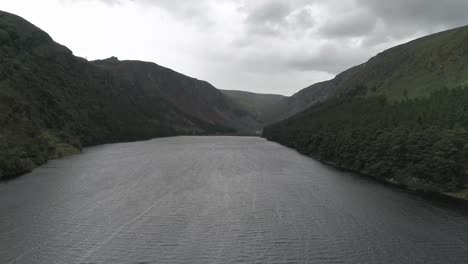 High-pullback-Panorama-view-Glendalough-Upper-Lake-surrounded-by-Mountains,-Wicklow