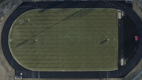 Rising-aerial-view-looking-down-at-lacrosse-field-with-track-circling,-4K