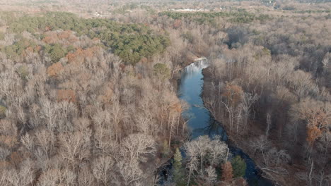 Quiet-River-Cutting-Through-Leafless-Forest-Landscape-In-Fall,-Aerial
