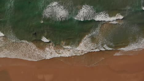 Relaxing-aerial-over-Malhão-beach,-gentle-waves-break-on-golden-sand