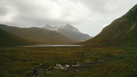 Hombre-Caminando-En-La-Naturaleza-Con-Una-Gran-Mochila-Explorando-La-Hermosa-Naturaleza-Verde-De-Escocia-Entre-Las-Altas-Montañas-Del-Cielo-En-Un-Día-Nublado