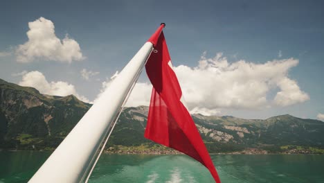 Shot-from-a-moving-boat-of-the-Swiss-flag-with-a-mountain-lake-in-background-in-4k