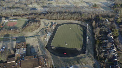 Aerial-view-orbiting-high-school-lacrosse-field-with-track-circling,-4K
