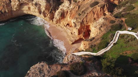 Aerial-drone-shot-over-beautiful-horse-shoe-shaped-beach-with-white-stairs-leading-to-the-beach-over-high-cliff