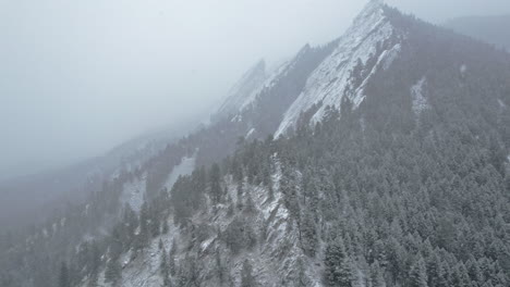 Drone-Aerial-Footage-Flying-Back-From-Pine-Tree-Snowcapped-Flatirons-Mountain-Near-Boulder-Colorado-USA-During-Snowstorm-Blizzard