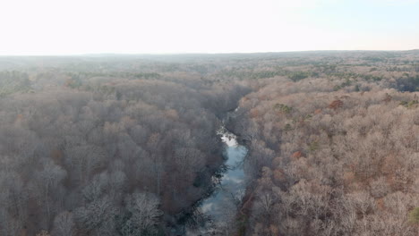 River-Mirroring-Cloudy-Sky-In-Leafless-Tree-Forest-Scenery,-Aerial