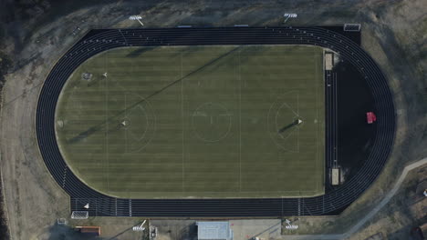 Top-down-aerial-descending-on-lacrosse-field-with-track-circling,-4K