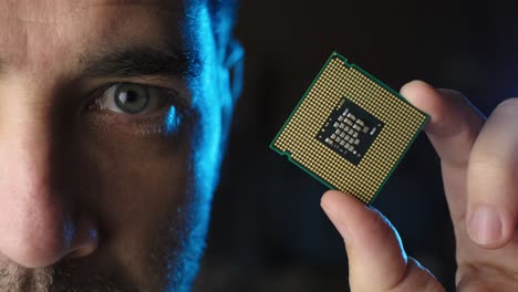 Männliches-Halbes-Gesicht-Mit-Blick-Auf-Den-CPU-Mikrochip-Prozessor-Auf-Seiner-Hand,-Schwarzer-Hintergrund