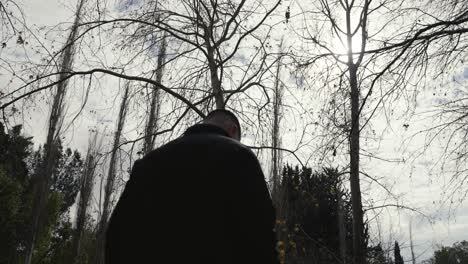 A-man-walking-alone-through-a-forest,-backlit-with-a-mysterious-and-moody-feeling