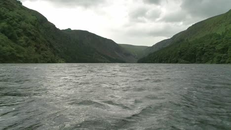 Drone-flying-low-Glendalough-Lake-water-surface,-wilderness-Landscape,-Wicklow-Mountains
