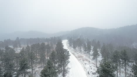 Drohne-Luftaufnahmen-über-Schneebedeckte-Landstraße-Umgeben-Von-Kiefern-In-Der-Nähe-Von-Flatirons-Mountain-In-Boulder-Colorado-Usa-Während-Eines-Nebligen-Schneesturms