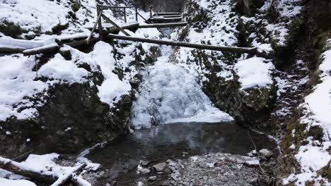 Wooden-Bridge-Over-A-Cold-Mountain-Stream-In-A-Winter-Forest---wide-shot