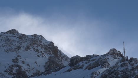 Nieve-Que-Sopla-Sobre-Montañas-Rocosas,-Gran-Altitud-En-Los-Alpes-Soleados---Vista-Inclinada