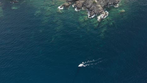 Aerial-follow-shot-of-the-small-white-boat-sailing-on-the-emerald-waters-near-Porto-Cervo,-Sardinia,-Italy