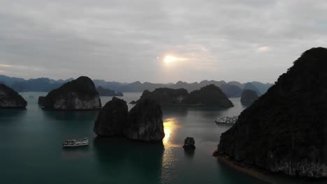 Aerial-sunset-of-Ha-Long-Bay-Vietnam,-little-rocky-islet-scenic-archipelago-with-cruise-yacht-boat-sailing-for-explore-and-excursion