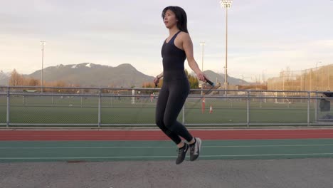 Gimbal-circling-shot-of-Asian-woman-in-workout-clothes-jumping-rope-outdoors