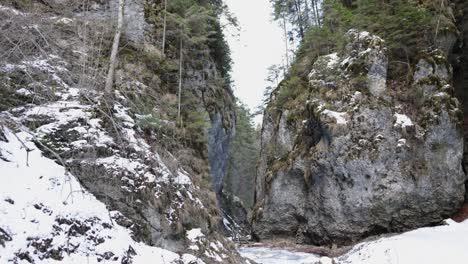Narrow-Gap-Between-High-Craggy-Mountains-In-Snow-Forest-At-Winter