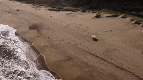 Aerial-tracking-shot-of-man-running-at-sandy-beach-during-sunny-day-in-Uruguay---Fitness-and-sport-lesson-outdoors-at-coast