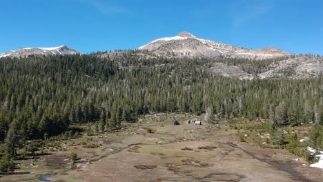 Drone-fly's-over-alpine-meadow-with-cabins-and-a-meandering-stream