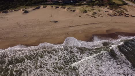 Aerial-view-of-person-entering-ocean-shoreline-with-foam-during-sunlight-at-beach---Cooling-in-water-during-hot-summer-day-in-Uruguay