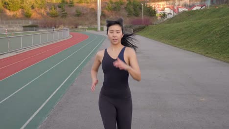 Mujer-Asiática-Corriendo-En-Pista-De-Atletismo-Acercándose-A-La-Cámara