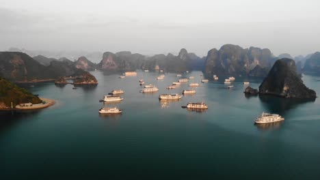 Scenic-aerial-view-of-Hạ-Long-Bay,-in-northeast-Vietnam,-cruise-yacht-luxury-boat-moored-at-sunrise-in-heavenly-bay-with-rocky-islets-and-clear-pristine-water
