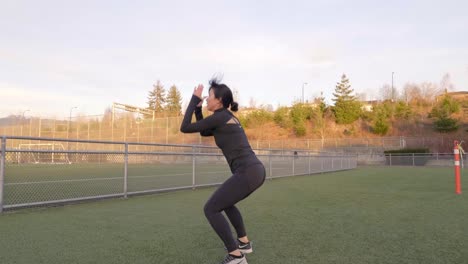 Asian-woman-in-workout-clothes-doing-squat-jumps-outdoors