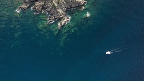 Aerial-follow-shot-of-the-small-white-yacht-traveling-on-the-emerald-waters-near-Porto-Cervo,-Sardinia,-Italy