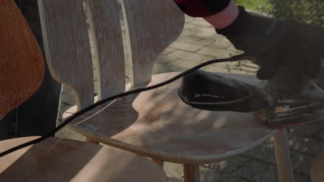 Detail-Shot-of-Handyman-Using-Polishing-Machine-To-Polish-Wood-and-refurbish-an-old-vintage-design-chair-in-the-garden-on-a-sunny-day-4K