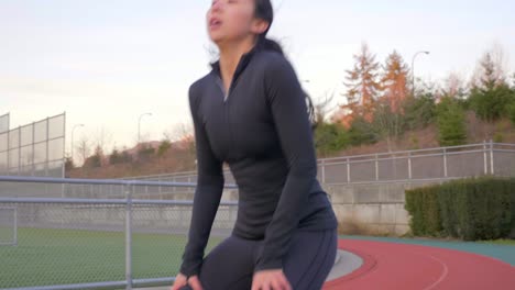 Tracking-shot-of-Asian-woman-running-on-athletics-track-and-stopping-to-rest