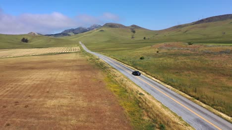 Black-Sedan-Car-Driving-On-The-Highway-Through-Lush-Fields-And-Hills-In-San-Luis-Obispo,-California