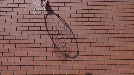 Front-on-slow-motion-shot-of-basketball-net-silhouette-shadow-as-ball-goes-into-ring-scoring-goal-on-red-brickwork-wall