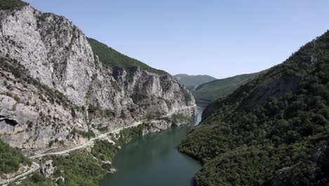 Drone-video-of-Plane-Discovery-ascending-over-the-Drin-River-at-the-Valbona-Pass-in-Kukes-County,-ending-up-showing-the-Ferry-stop-at-Komani-with-a-boat-sailing