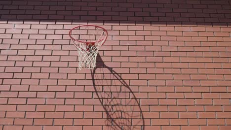 Vordere-Breitere-Aufnahme-Des-Roten-Basketballrings-An-Der-Ziegelwand,-Wobei-Der-Ball-Zum-Swish-Ins-Tor-Geht
