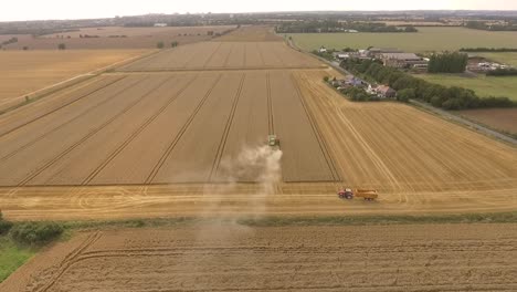 Harvest-drone-approach-then-pan-down-over-combine-harvester,-tractor-and-countryside-in-view
