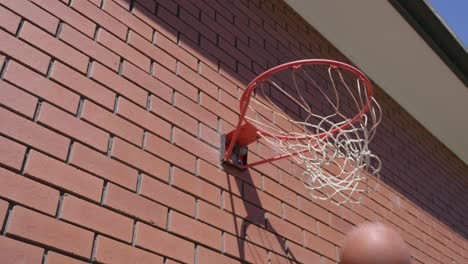 Side-perspective-of-basketball-circling-around-basketball-ring-in-slow-motion-before-going-through-net-for-a-goal-with-red-brick-wall-background