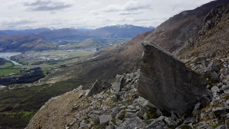 Rock-climber-high-up-in-the-mountains-on-a-cloudy-day-in-Queenstown,-New-Zealand