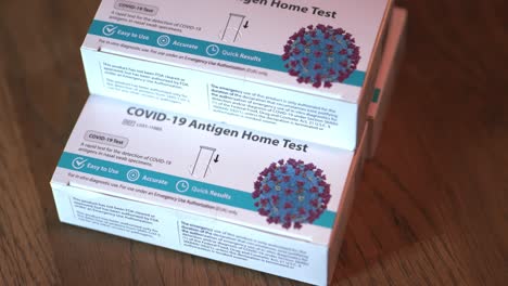 Covid-19-at-home-Antigen-test-kit-for-coronavirus-3-white-and-blue-boxes-of-tests-stacked-up-wide-shot-focusing-on-top-and-bottom-boxes-and-slowly-panning-around-table