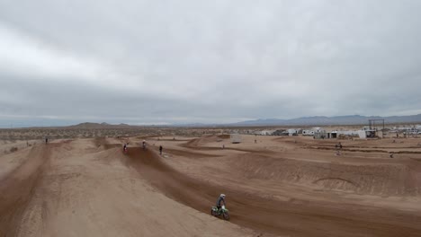 Motorcycles-taking-high-jumps-as-they-fly-around-a-racetrack-in-the-Mojave-Desert---leading-aerial-view