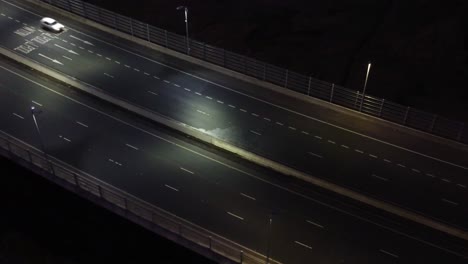 Illuminated-aerial-view-above-vehicles-driving-highway-traffic-lanes-at-night-pan-left-tilt-up