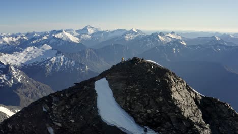 Mann,-Der-Auf-Dem-Gipfel-Eines-Riesigen-Berges-Mit-Felsen-Und-Schnee-Auf-Dem-Gipfel-Inmitten-Einer-Spektakulären-Bergkette-Hoch-über-Den-Tälern-In-Neuseeland-Während-Des-Sonnenaufgangs-Steht