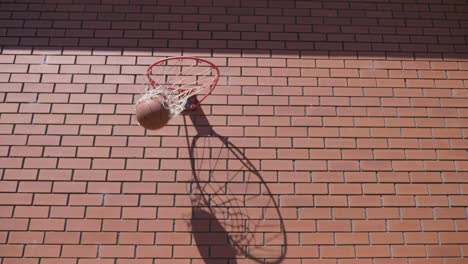 Front-perspective-of-basket-ball-circling-around-metal-ring-and-goes-into-hoop-for-goal-on-red-brick-wall-background