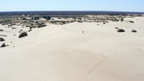 Girl-exploring-huge-sand-dunes-in-an-Australian-desert-on-a-hot-bright-sunny-day,-aerial-shot-2