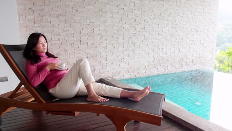 Asian-woman-relaxing-on-a-pool-bed-and-drinking-coffee-by-her-private-pool-during-her-morning-vacation