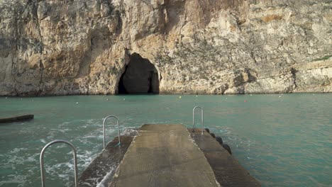 Caminar-Sobre-Un-Muelle-De-Piedra-Cerca-De-Cuevas-Marinas-Interiores-Con-Olas-Del-Mar-Mediterráneo-Rompiendo-Desde-Los-Lados