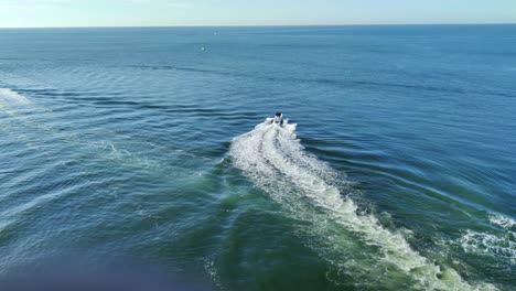 A-speed-boat-moving-fast-in-middle-of-the-sea-with-a-beautiful-trail-in-water-drone-shot-|-Aerial-view-of-a-speedboat-moving-in-middle-of-the-sea-video-background-in-4K
