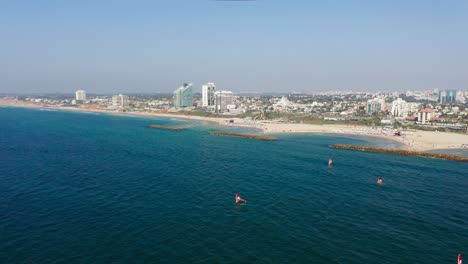 Several-windsurfers-surf-the-clear-blue-waters-of-the-Mediterranean-towards-the-breakwaters-with-in-the-background-the-touristic-city-Herzeliya-in-Israel
